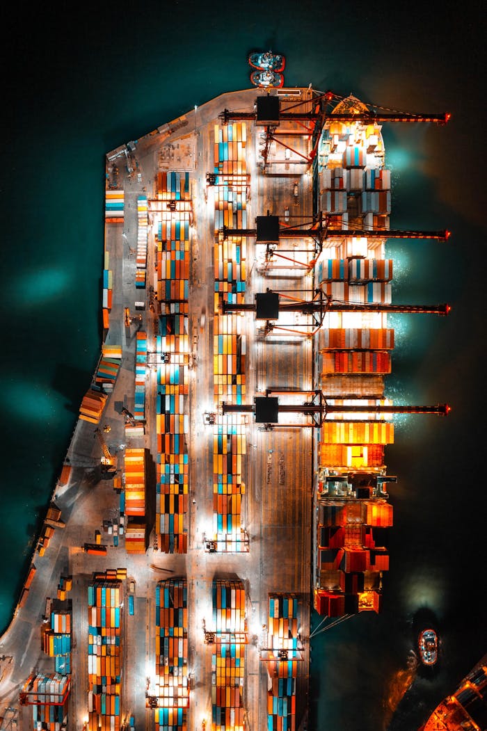 about-02 Dramatic aerial view of a busy shipping port with colorful containers and bright lights at night.